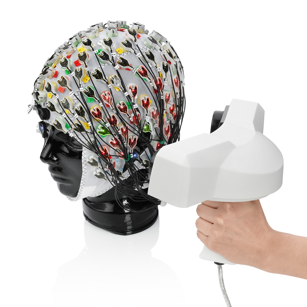 Side view of P CapTrak EEG cap on mannequin head with multicolor electrode layout, shown with TMS coil positioned for compatibility demonstration