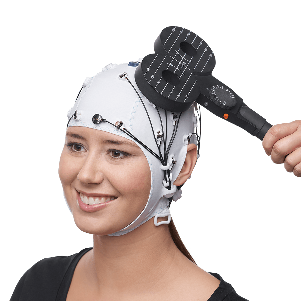 Smiling participant wearing a white EEG cap with actiCAP slim electrodes, while a hand holds a figure-eight transcranial magnetic stimulation (TMS) coil against their scalp