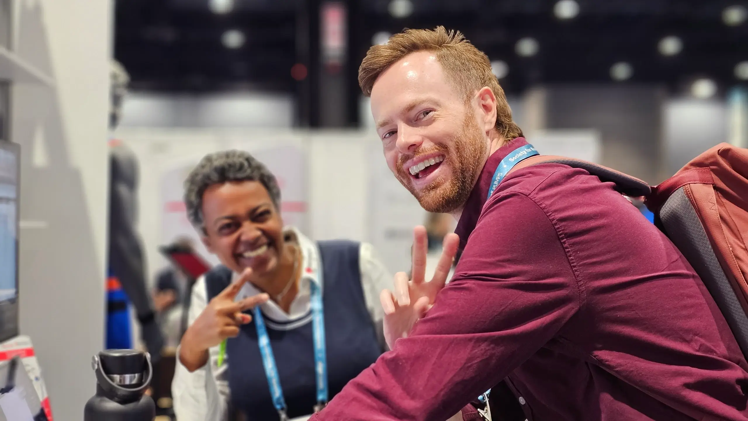 Two Brain Vision team members smiling and flashing peace signs at a conference booth