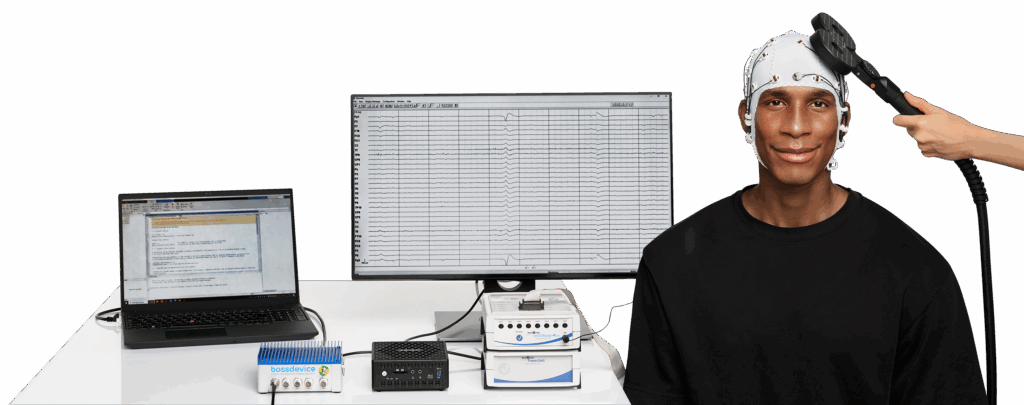 A participant sits wearing an EEG cap while a TMS coil is held to the side of their head. Behind them are two computer screens showing realtime EEG data as recorded and processed by the actiCHamp Plus, TurboLink, and bossdevice RESEARCH that sit on the table.