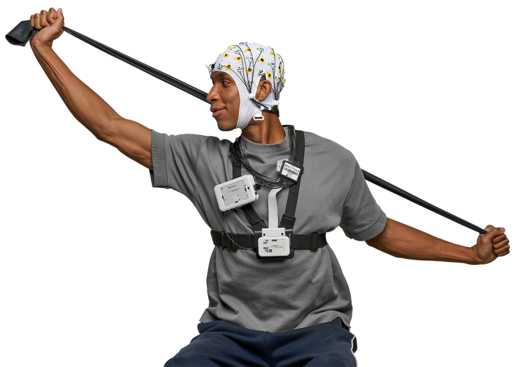 A male participant is depictred doing stretching with an exercise band while wearing an actiCAP snap EEG cap and a chest harness across his front that holds a LiveAmp, actiCAP slim electrode bundle, and a LiveAmp Sensor & Trigger Extension Compact (STEc).